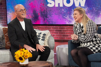 Howie Mandel and Kelly Clarkson laughing on the couch of the Kelly Clarkson Show