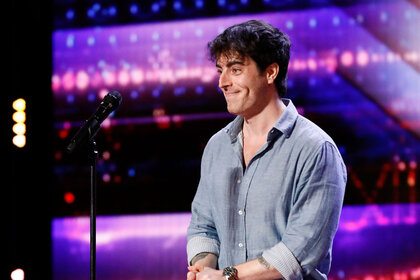 Sam Cieri standing on the AGT stage with a smile on his face