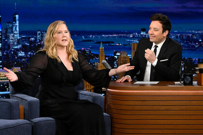 Amy Schumer speaks wearing all black as host Jimmy Fallon looks on on The Tonight Show Starring Jimmy Fallon.