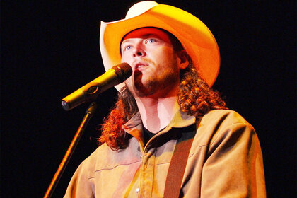 Blake Shelton performs on stage in a cowboy hat and curly long hair