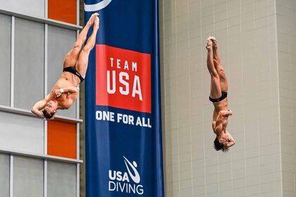 Gregory Duncan and Tyler Downs dive past a Team USA banner.