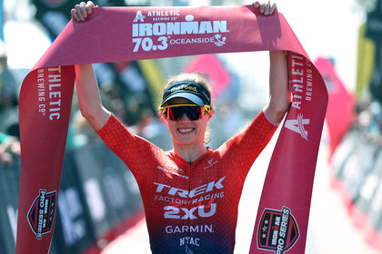 Taylor Knibb smiling and holding up a banner from an Ironman race.