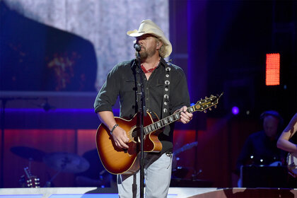 Toby Keith wears a cowboy hat on stage while he plays guitar and sings