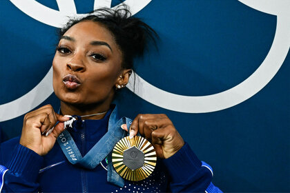 Simone Biles holds up her diamond goat necklace after winning the artistic gymnastics women's all around final of the Paris 2024 Olympic Games at the Bercy Arena in Paris, on August 1, 2024.