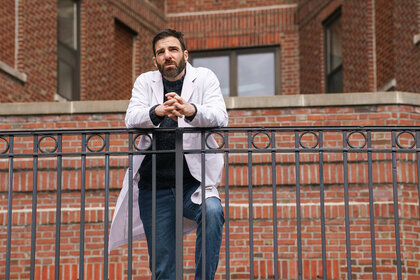 Dr Oliver Wolf leans on a railing outside of a brick building on Brilliant Minds 101