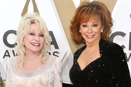 Dolly Parton and Reba McEntire smile together on the red carpet.