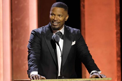 Jamie Foxx speaks onstage in a suit.