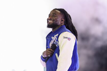 Shaboozey smiles in a blue and white NFL letterman jacket.