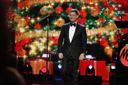 Michael Buble smiles in a tuxedo in front of Christmas decorations.