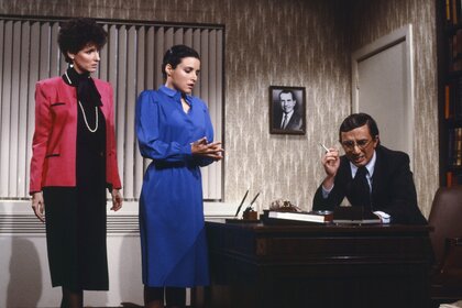 Mitsy Cooper (Mary Gross) and Ms. Kirk (Julia Louis-Dreyfus) stand next to Nathan Thurm (Martin Short) who sits at a desk during a skit on Saturday Night Live.