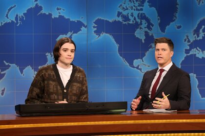 Jane Wickline and Colin Jost sitting behind a desk in front of a map.