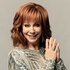 Reba McEntire smiling and looking at the camera with her hands joined near her face.