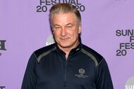 Alec Baldwin, wearing a navy sweater, looking at the camera with a slight smile.