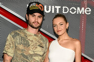 Chase Stokes wears a camo shirt and baseball hat next to Kelsea Ballerini in a white shirt