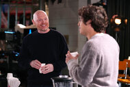 Bill Burr talks to Marcello Hernández while holding a drink during promos for SNL Season 50 Episode 6