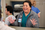 Val holds her hands up and looks happy on St. Denis Medical Season 1 Episode 1.