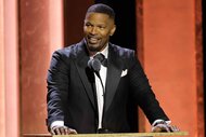 Jamie Foxx speaks onstage in a suit.