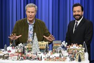 Will Ferrell and Jimmy Fallon sit behind a Christmas Village.