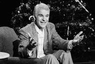 Steve Martin sits in a chair in front of a christmas tree on Saturday Night Live