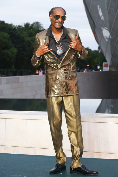 Snoop Dogg wears a gold suit and opens his jacket to show his globe chain at the prelude to the olympics