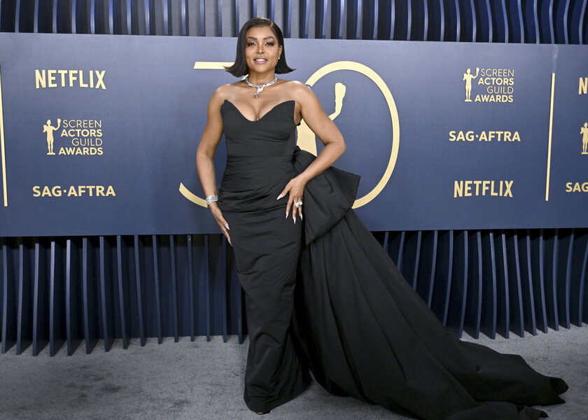 Taraji P. Henson posing in a black gown in front of a step and repeat.