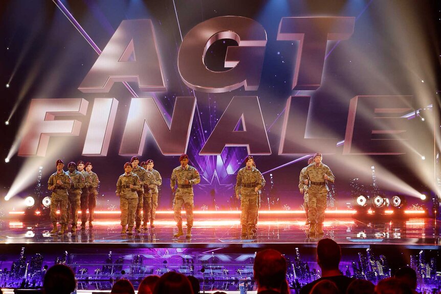 82nd Airborne Division Chorus performing together on stage in front of a large sign that says AGT Finale.