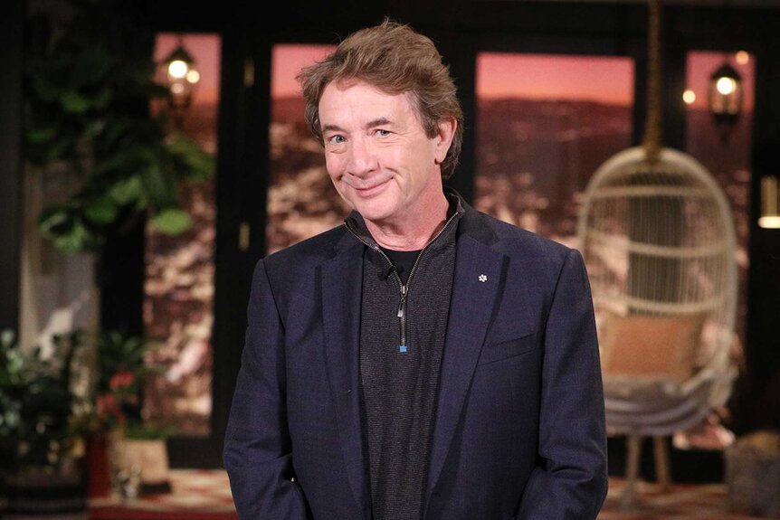 Martin Short wears an all black outfit and smiles at the camera.