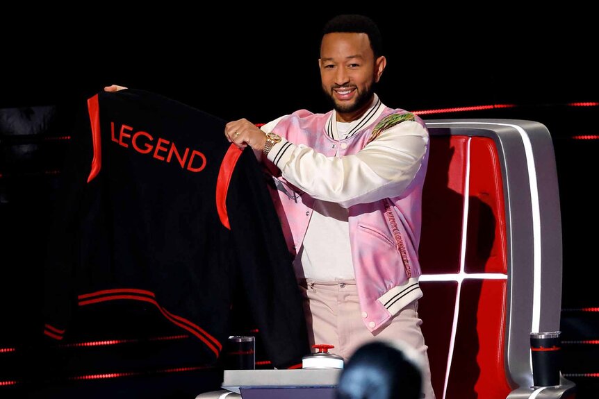 John Legend holds up a "Legend" jersey in Season 25 Episode 4 of The Voice.