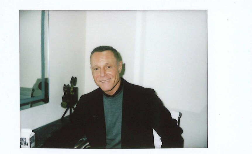 An instax of Jason Beghe sits in a chair in a green room