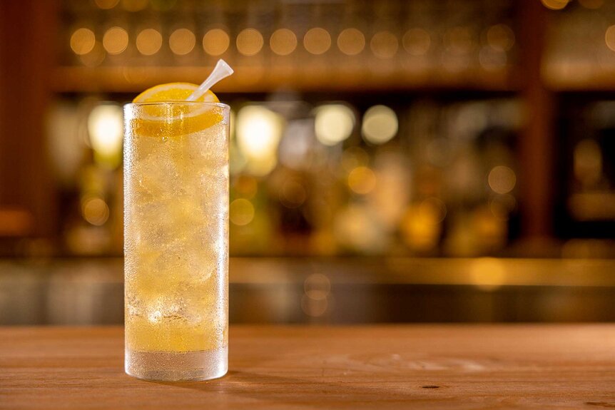 A clear drink in a thin glass with lemons on a wooden bar with the background out of focus