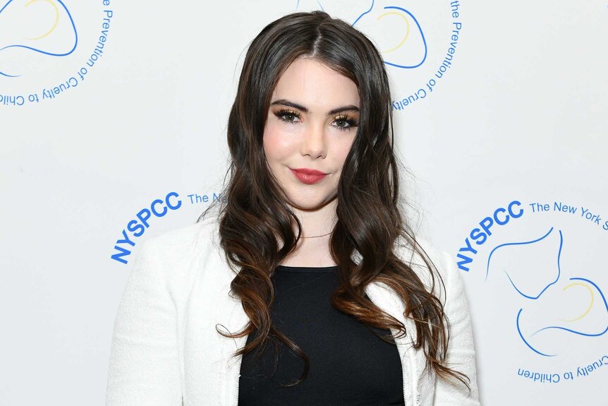 Mckayla Maroney wears a black dress and white sweater during an event