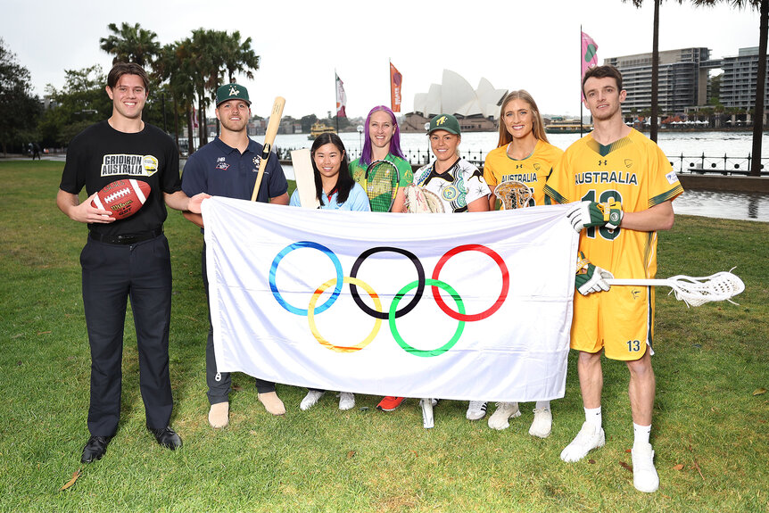 Atheletes hold up a flag with the olympic rings on it in Australia