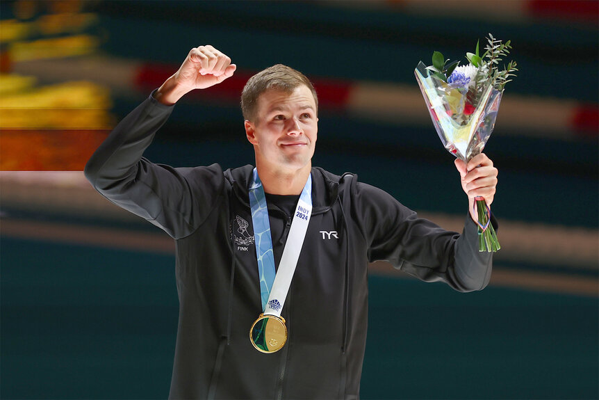 Nic Fink holds up flowers and his fist celebrating his gold medal for winning the Men's 100 Meter Breaststroke Championship