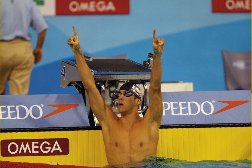 Michael Phelps raises his arms and points his fingers in a pool.