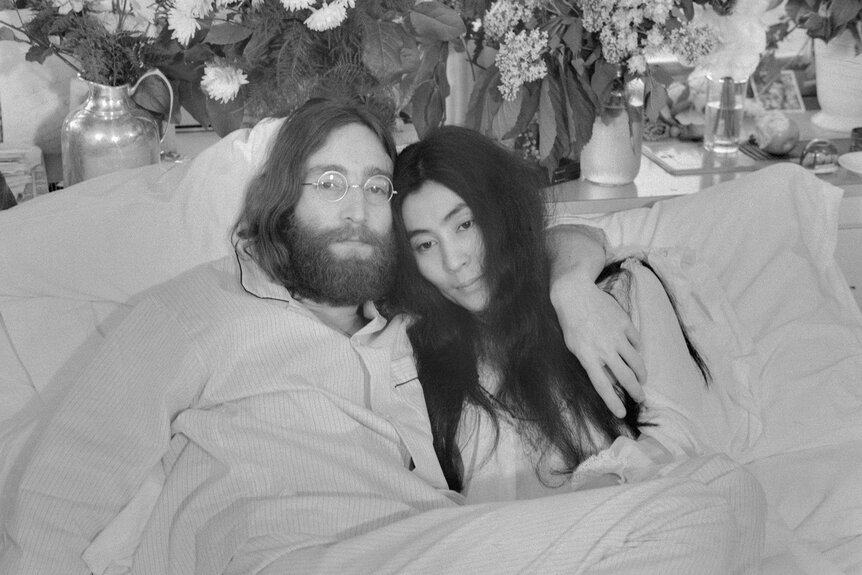 John Lennon and Yoko Ono pose together in bed surrounded by flowers