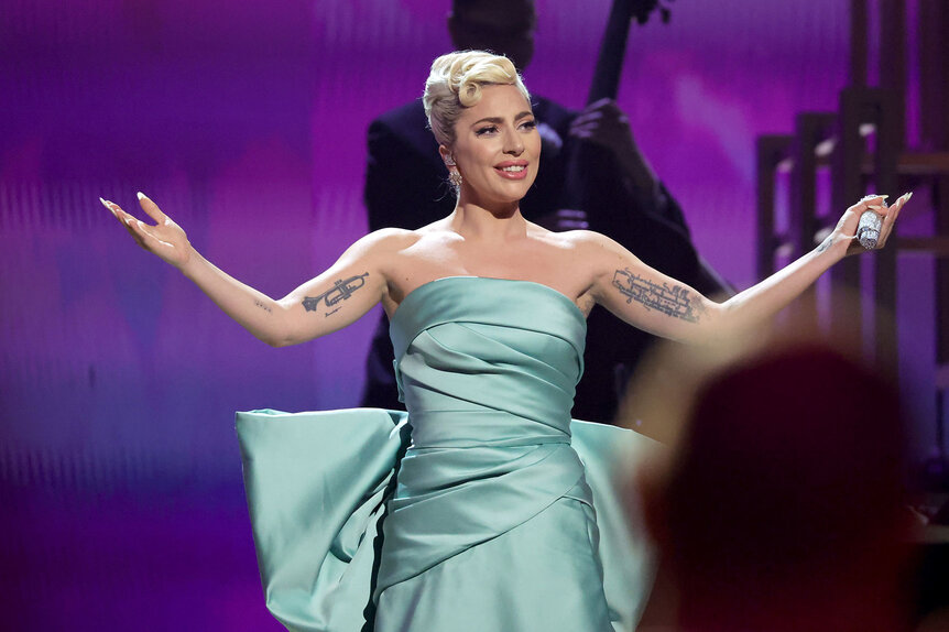 Lady Gaga smiling on stage in a gown.