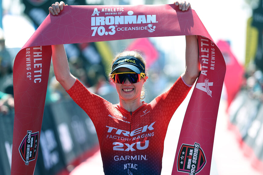 Taylor Knibb smiling and holding up a banner from an Ironman race.