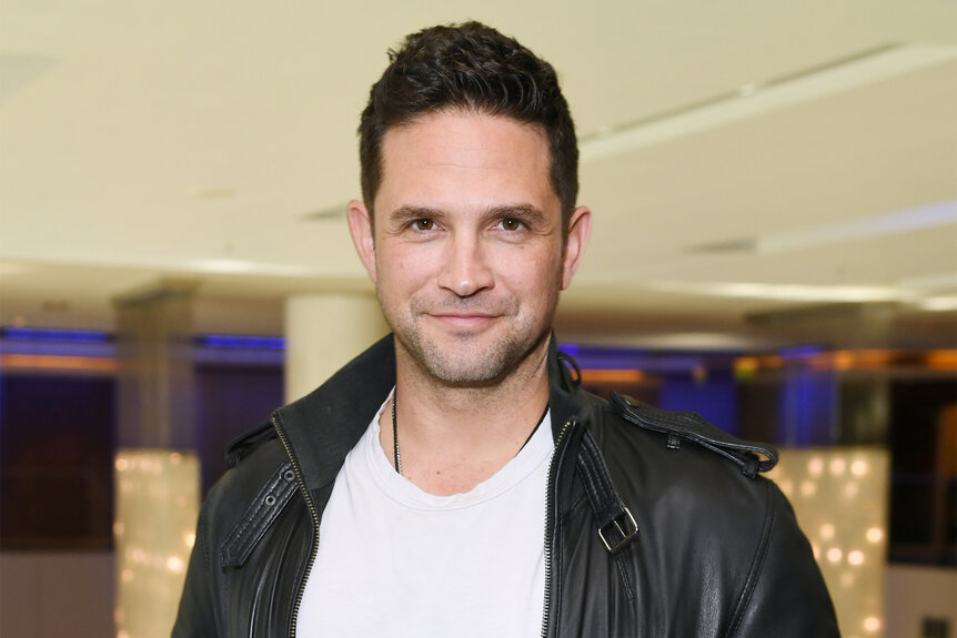 Brandon Barash wears a leather jacket and white shirt at a fan event