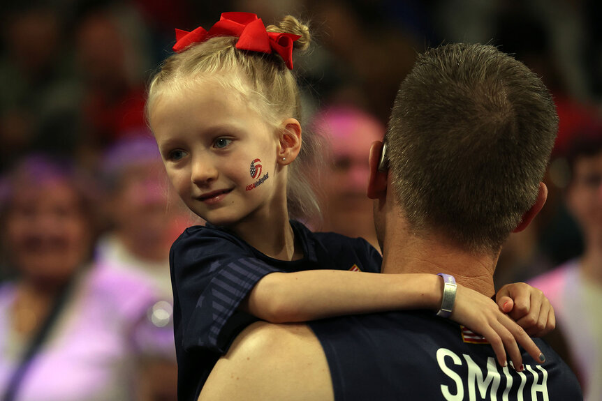 David Smith of Team United State carries daughter Amelia after the Men's Preliminary Round Pool C volleyball match between Team United States and Team Germany