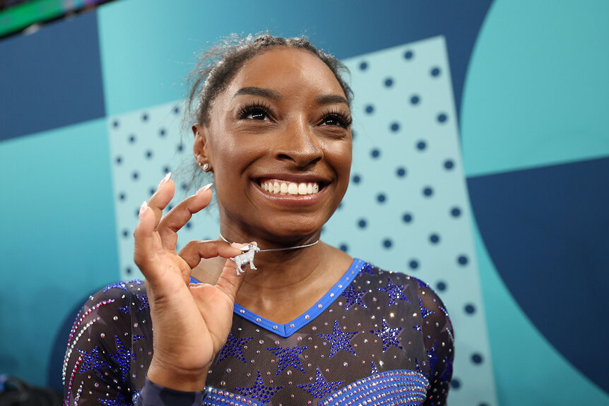 Simone Biles holds up her diamond goat necklace after winning the artistic gymnastics women's all around final of the Paris 2024 Olympic Games at the Bercy Arena in Paris, on August 1, 2024.