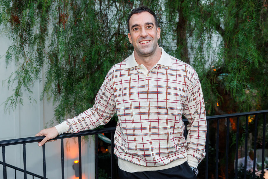 Michael Grassi poses for a photo in front of a staircase with plants hanging behind him