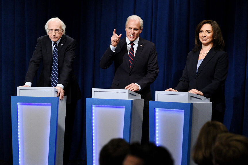 Larry David as Bernie Sanders, Woody Harrelson as Joe Biden, and Maya Rudolph as Kamala Harris stand at podiums during the "DNC Town Hall" sketch