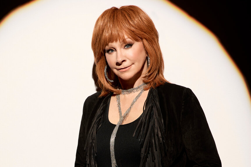 Reba Mcentire smiles wearing a black fringe jacket for the voice season 26