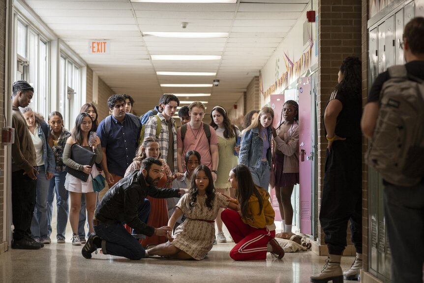 Dr. Oliver Wolf (Zachary Quinto) tends to Sarah Kim (Amalia Yoo), who sits on the ground as high schoolers watch, on Brilliant Minds Episode 106.