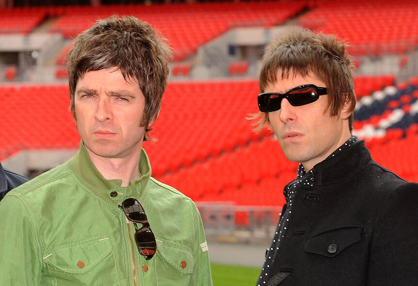 Oasis' Noel Gallagher and Liam Gallagher pose together in a stadium.