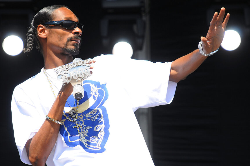 Snoop Dogg wears a white t-shirt and large ring on stage while performing