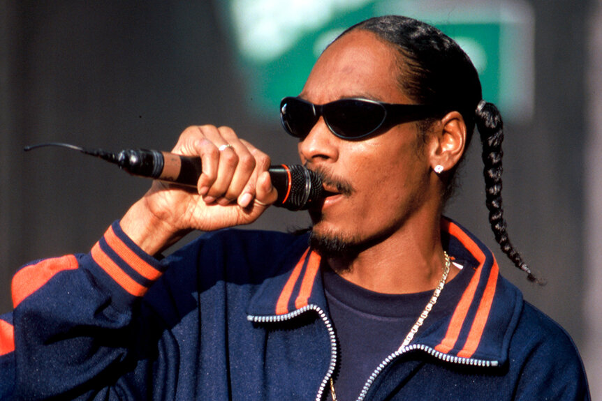 Snoop Dogg wears an orange and blue jacket on stage while performing