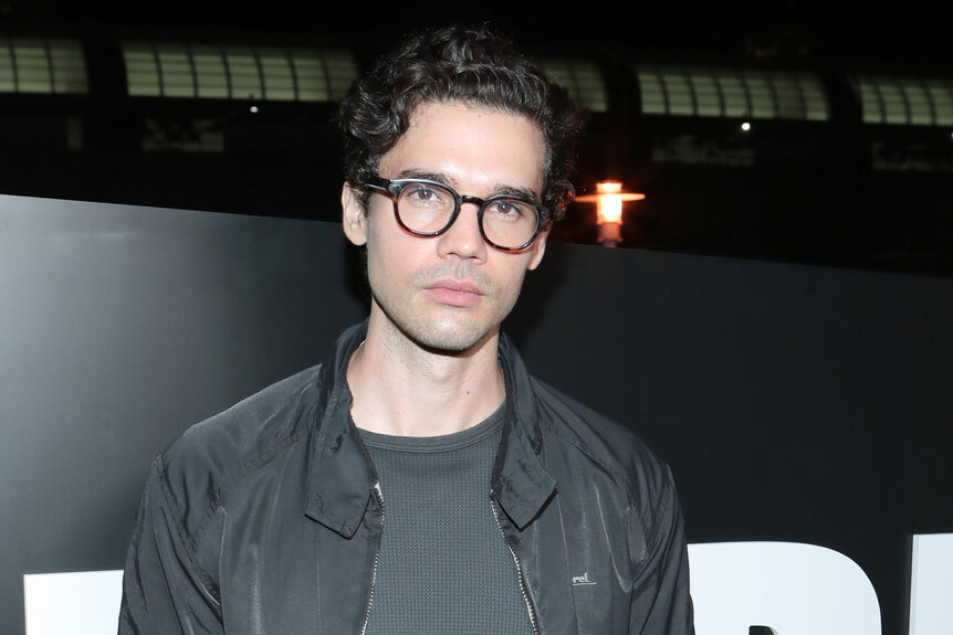 Steven Strait wears a grey jacket and glasses at a party