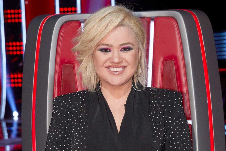 Kelly Clarkson sits in her coaches chair with blonde hair on the voice season 18 episode 2