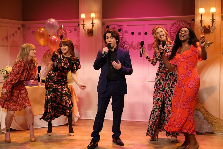 SNL cast members dancing while holding microphones.